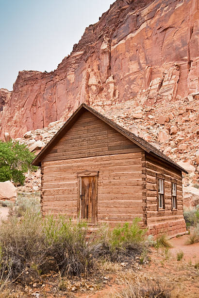Historic Fruita School Capitol Reef National Park is in the desert of southern Utah. The park is filled with cliffs, towers, domes and arches. The first part of the park’s name derives from the many dome shaped Navajo Sandstone formations each of which resembles the US capitol. The second half of the name refers to the parallel impassable ridges which the early settlers called reefs. The first paved road through this area wasn’t constructed until 1962. Central to the area is the famous Waterpocket Fold, a 100-mile wrinkle in the earth, which is 65 million years old and the largest exposed monocline in North America. The Fremont River has carved canyons through some parts of the Waterpocket Fold but the area remains a dry desert. The park is also a showcase for ancient history and the more recent history of the Mormon pioneers. The Elijah Cutler Behunin family, early settlers of the Fruita area, donated the land for a school in 1892. When the school was built, it had a dirt roof and bare walls. In 1935 the walls were chinked in. Elijah’s daughter, Nettie, was the school's first teacher. The Fruita School functioned as a grade school until 1941. In 1973 the school was listed on the U.S. National Register of Historic Places. This scene of the school was photographed in Capitol Reef National Park in Fruita, Utah, USA. jeff goulden capitol reef national park stock pictures, royalty-free photos & images