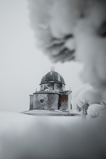Hitoric chapel on Mount Radhost in Pustevny in Beskydy mountains in the east of the Czech Republic. Minimalism. The chapel rises out of the white mist. Wooden Catholic chapel shaved by frost and snow.
