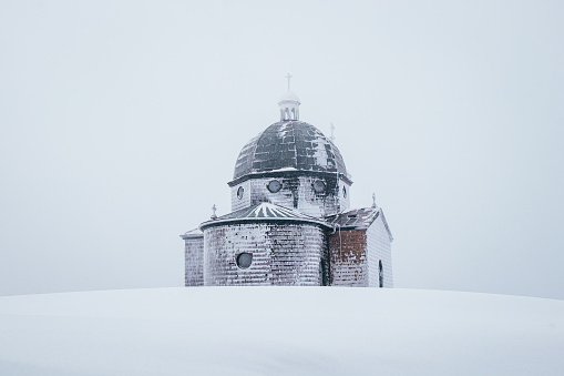 Hitoric chapel on Mount Radhost in Pustevny in Beskydy mountains in the east of the Czech Republic. Minimalism. The chapel rises out of the white mist. Wooden Catholic chapel shaved by frost and snow.