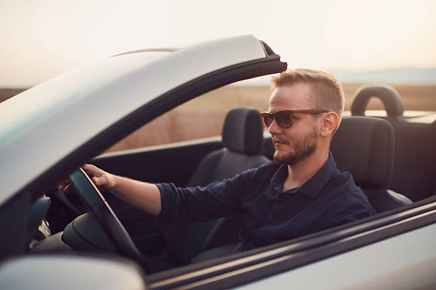Hitting The Road Young caucasian man driving a convertible. luxury car stock pictures, royalty-free photos & images