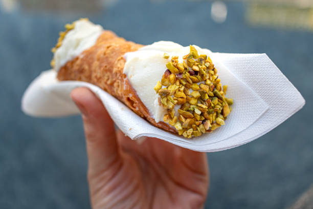 Holding a cannoli A hand holding a traditional pistachio topped cannoli in the streets of Milan. cannoli stock pictures, royalty-free photos & images