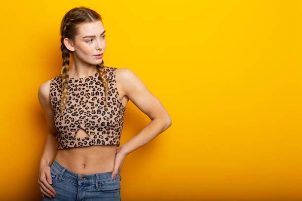 Holding hand on hip, a smiling attractive blonde young woman against yellow background with copy space, dressed in crop top with tiger print stock photo