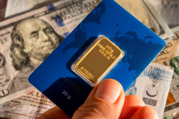 Holding one 20 g fine gold ingot over mixed Turkish and American cash money currency Global Financial Concept: Combination of mixed American US-Dollar currency, one hundred Turkish money, TL paper banknotes from Turkey and gold ingots. International stock market exchange rates as economic background with copy space. gold bar stock pictures, royalty-free photos & images