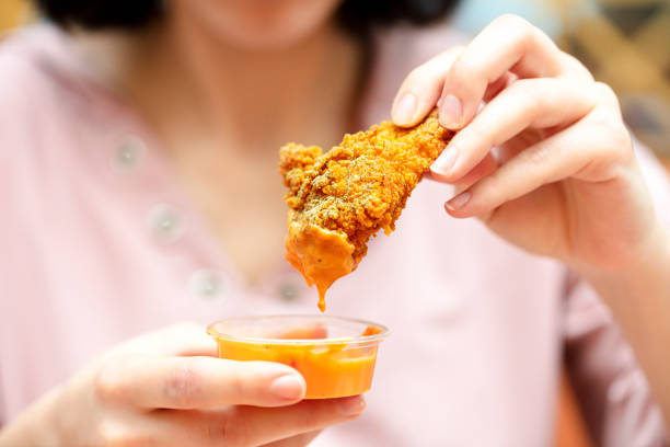 Holding the fried chicken, dip it into the sauce. fast food restaurant. stock photo