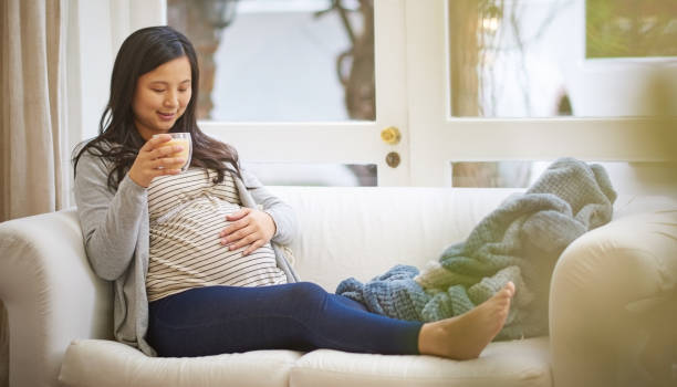 Holding the promise of a new life Shot of an attractive young pregnant woman drinking an iced coffee while relaxing on the sofa at home caffeine pregnancy stock pictures, royalty-free photos & images