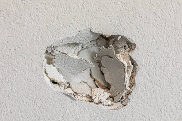 A hole in the wall of a hallways caused by a fist punching through the wall stock photo