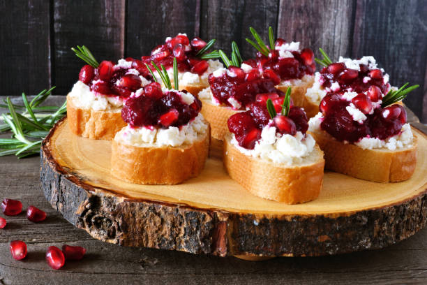 Holiday crostini appetizers with cranberries, pomegranates and feta on a wood log platter Holiday crostini appetizers with cranberries, pomegranates and feta cheese on a rustic wood log platter crostini photos stock pictures, royalty-free photos & images