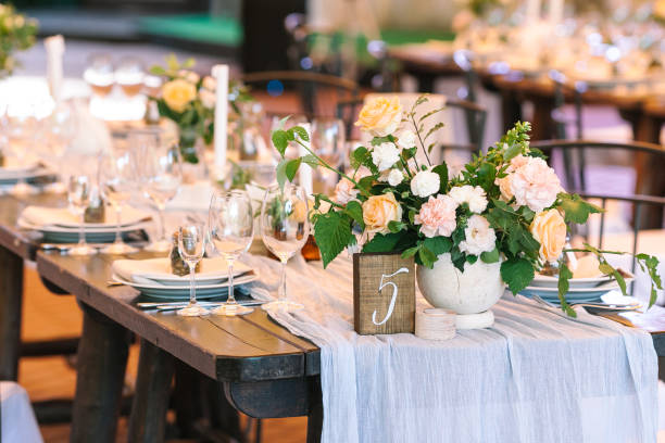 holiday, excitement, serving concept. there are untouched white dishes, clear wineglasses, silverware and gorgeous bouqets of roses avalanches on the table numbered five stock photo