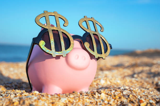 Holiday savings pink piggy bank on a beach vacation with dollar sign sunglasses Holiday savings piggy bank on a beach vacation with sunglasses bringing home the bacon stock pictures, royalty-free photos & images