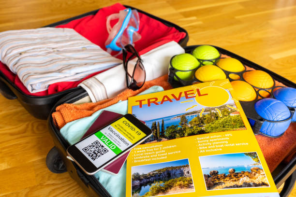 Holiday suitcase with beach travel brochure and mobile phone showing vaccination certificate along with paper passport stock photo