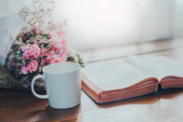 Holy bible with a cup of coffee and flowers on wooden table against window light, Christian background with copy space stock photo