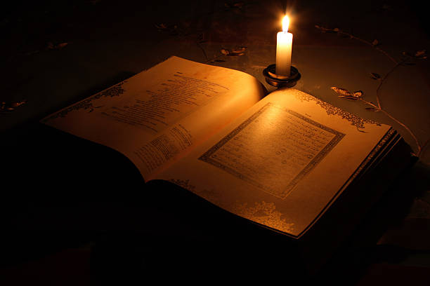 Holy Koran laying open on a desk with one lit candle stock photo