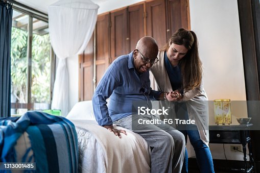 istock Home caregiver helping a senior man standing up at home 1313001485