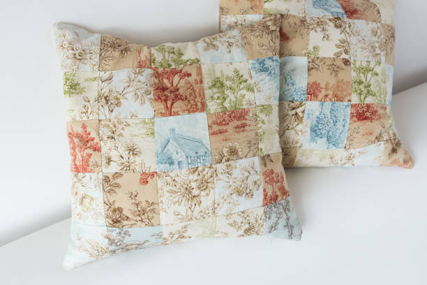 home cosiness, handcraft, sewing, patchwork concept - two decorative cushion made of patches in pastel shades with tender floral prints and image of country house stock photo