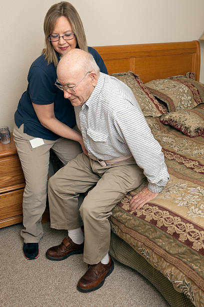 Home Healthcare Worker Using Gait Belt to Assist Patient A female home healthcare worker is using a gait transfer belt to assist a patient from a bed. Today various aspects of bringing medical care to the home are gaining in popularity. belt stock pictures, royalty-free photos & images