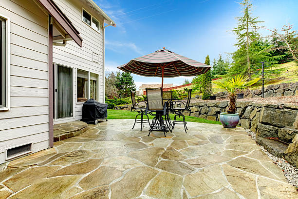Home patio area overlooking beautiful landscaping Concrete floor cozy patio area with iron table set and patio umbrella. Patio area surrounded by green terrace landscaping patio stock pictures, royalty-free photos & images