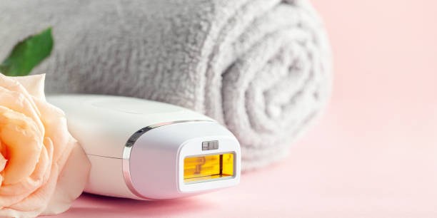 Home spa accessories -  photoepilator on pink  background. Apparatus and rose as a symbol stock photo