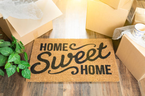Home Sweet Home Welcome Mat and Moving Boxes on Hard Wood Floor stock photo