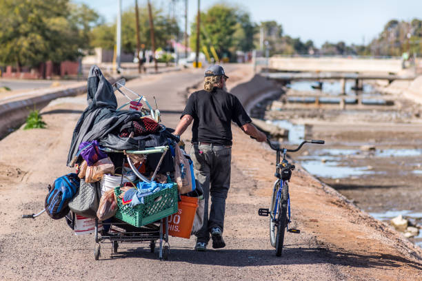 Homeless Man Pulling Cart A homeless man in Phoenix pulls an overladen shopping cart along a path next to the Arizona Canal. At the time of the photo the canal was drained for cleaning. scavenging stock pictures, royalty-free photos & images