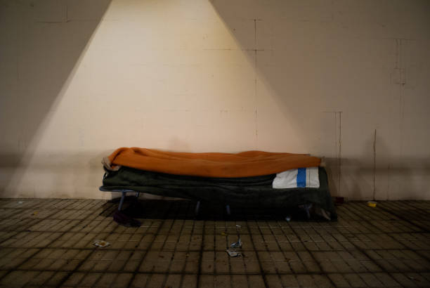 Homeless person's bed with an orange blanket on sidewalk stock photo