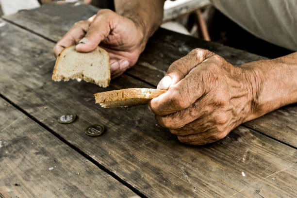 Homeless. Poverty in retirement. Hands the poor old man's, piece of bread and change, pennies on wood background. The concept of hunger or poverty. Selective focus. stock photo