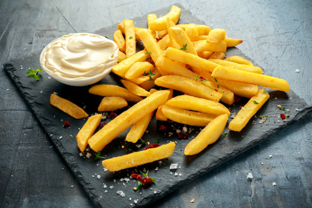 hausgemachte gebackene pommes frites mit mayonnaise, salz, pfeffer auf schwarzen steinplatte - chips potato stock-fotos und bilder
