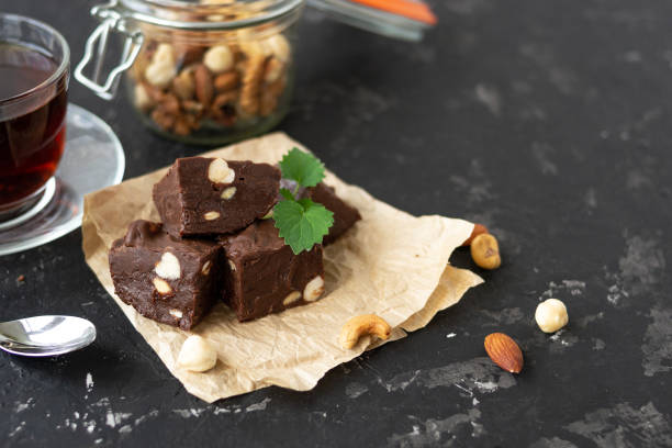 Homemade chocolate fudge garnished with mint leaves and served with tea on a black background. Nuts in the background blurred background. Copy space. stock photo
