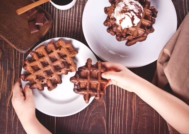 Homemade chocolate waffles with ice cream decorated chocolate syrup. Child hand take a one waffle. Top view. stock photo