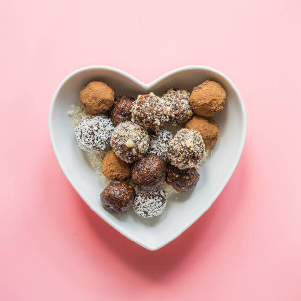 Homemade energy balls with cacao, nuts, and coconut flakes in plate as heart on pink. Concept healthy sweet food. Vegan dessert. Homemade natural energy balls with cacao, nuts, and coconut flakes in plate as heart on pink. Concept healthy sweet food. Vegan dessert. plasma ball stock pictures, royalty-free photos & images