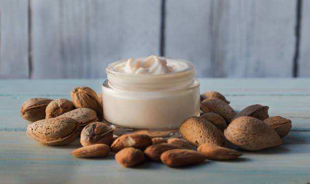 Homemade facial cream of almond oil surrounded by natural almonds Homemade facial cream of almond oil surrounded by natural almonds, n a white wooden background almond butter stock pictures, royalty-free photos & images
