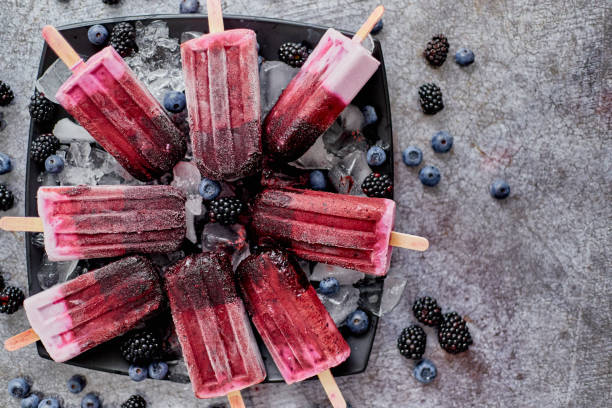 Homemade fresh frozen blueberry and blackberry popsicles on black plate with ice sitting on stone stock photo