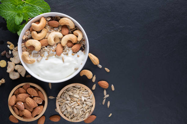 Homemade granola or muesli, bowl of oat granola with yogurt, almond, Cashew nuts, mint and nuts on the black rock board for healthy breakfast, copy space. Healthy breakfast menu concept. stock photo
