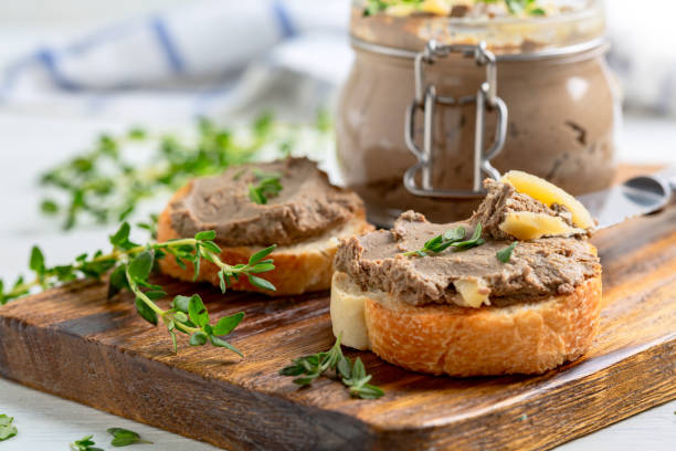 Homemade pate on baguette slices. Slices of toasted baguette with turkey pate with thyme and a jar of pate are served on a wooden service board. Concept of delicious homemade food. liver pâté photos stock pictures, royalty-free photos & images