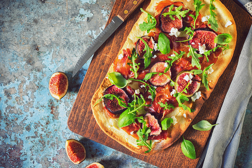 Homemade pizza with figs, prosciutto, arugula and goat cheese