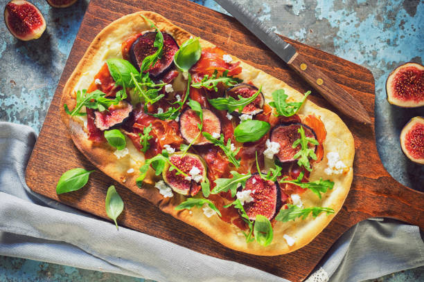 Homemade pizza with figs, prosciutto, arugula and goat cheese stock photo