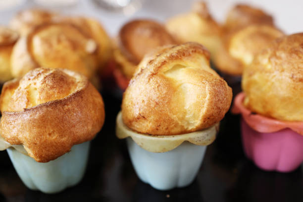 Homemade popover, which is a lush, airy and egg hollow roll, fresh from the oven. Yorkshire pudding freshly baked in silicone blue and pink baking dishes, selective focus stock photo