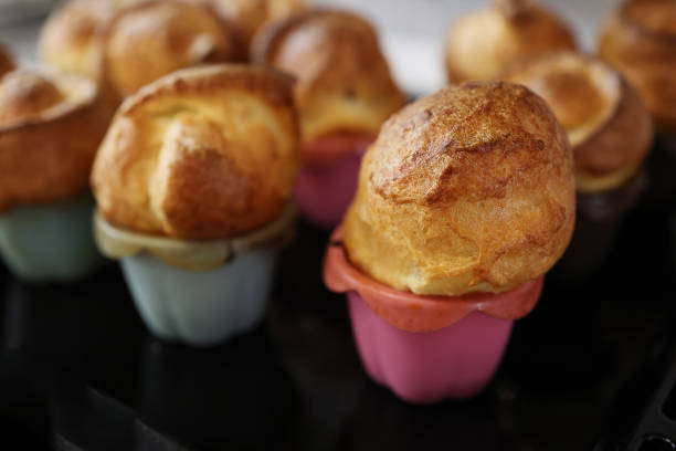 Homemade popover, which is a lush, airy and egg hollow roll, fresh from the oven. Yorkshire pudding freshly baked in silicone blue and pink baking dishes, selective focus stock photo