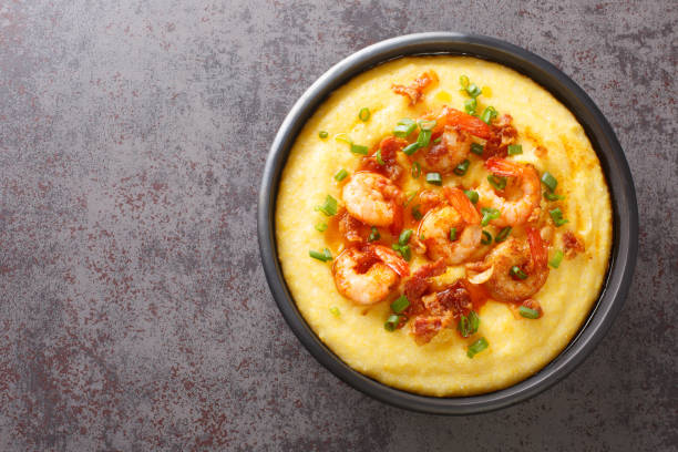 Homemade shrimp and grits with smoked bacon, onions and cheese in a black bowl on a dark concrete background. Horizontal top view stock photo