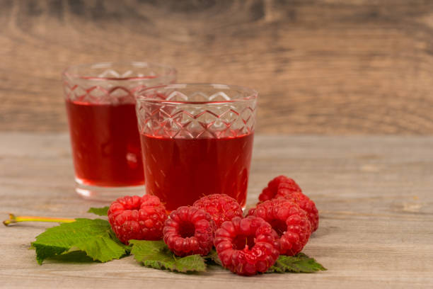 homemade sweet raspberry wine or juice in small glasses with fresh berries on aged wooden table stock photo