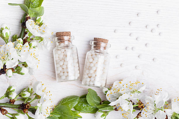 homeopathic pills with spring flowers on white wooden background homeopathic pills with spring flowers on white wooden background homeopathic medicine stock pictures, royalty-free photos & images