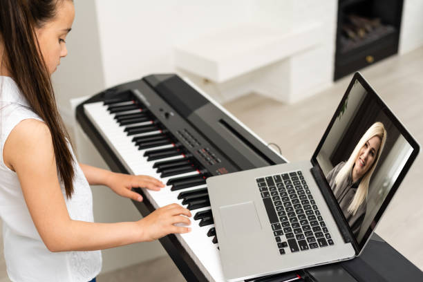 Homeschool little young kid girl learning piano from computer connecting to internet music online class by school teacher. New normal lifestyle and education, student study at home concept. stock photo