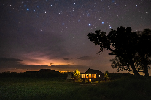 An 1800's homestead with storm clouds and stars above at night.