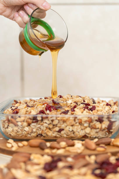 Honey falling on a bowl full of granola and dried fruit Vertical photo with selective focus of honey falling on a bowl full of granola and dried fruit in a kitchen with a white background hot peruvian women stock pictures, royalty-free photos & images