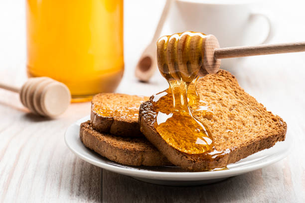 honey Honey dripping from wooden dipper on some wholemeal rusks. toasted bread stock pictures, royalty-free photos & images