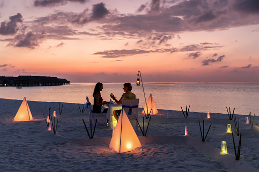 Couple is having a private event dinner on a tropical beach during sunset time: Honeymoon travel concept