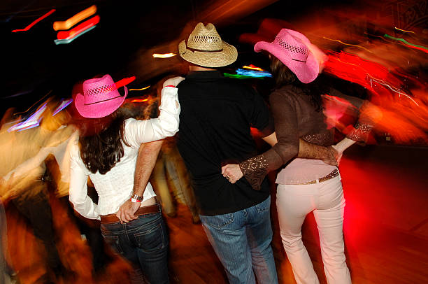 Honky Tonk Country Dancing Threesome A guy and two cowgirls dance in a country western honky tonk bar with neon lights blurred in the background. Shot with slow shutter speed to accentuate motion and action in the scene. country and western music stock pictures, royalty-free photos & images