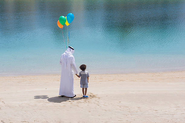 Hope for the future generations Middle Eastern grandfather with his grandson in the beach, conceptual image of an Emirati grandfather holding balloons with his grandson holding hands in the beach. old arab man stock pictures, royalty-free photos & images