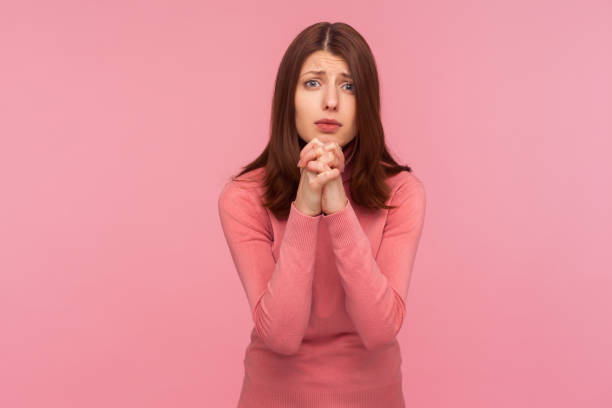 Hopeful brunette woman in pink sweater holding hands in prayer, asking for forgiveness looking at camera with regard, need help Hopeful brunette woman in pink sweater holding hands in prayer, asking for forgiveness looking at camera with regard, need help. Indoor studio shot isolated on pink background prayer request stock pictures, royalty-free photos & images