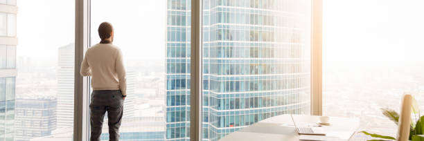 horizontale bild-rückansicht geschäftsmann steht mit blick durch panoramafenster - penthouse stock-fotos und bilder