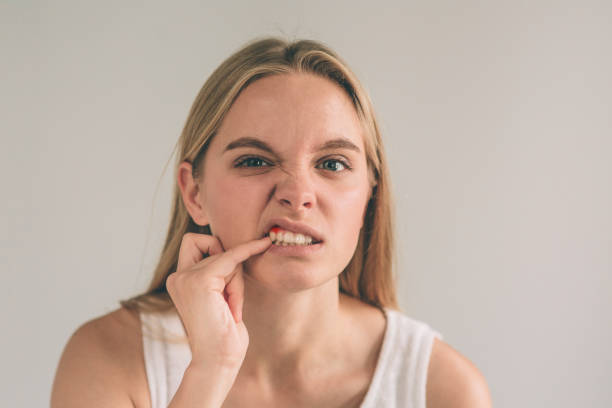 A horizontal photo of a young worried woman in checkered shirt suffering from strong toothache and touching her cheek stock photo